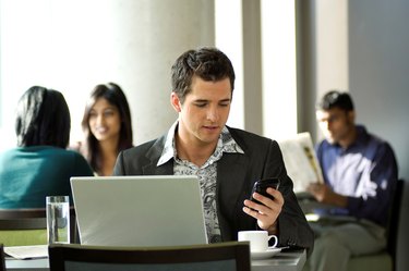 Young urban businessman using Blackberry PDA and wireless laptop in a hotspot cafe.