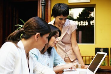 Three women having meeting in restaurant looking at laptop