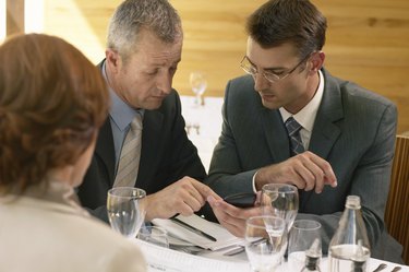 Two businessmen and businesswoman in restaurant, men using calculator