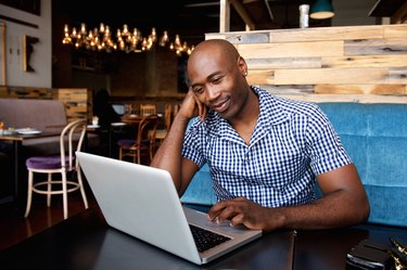Relaxed african man at a cafe table using laptop
