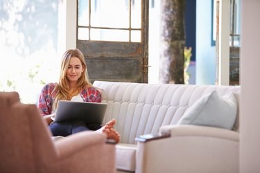 Woman Relaxing On Sofa At Home Using Laptop Computer