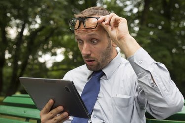 Businessman at the park with tablet sitting on a bench.