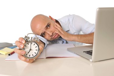 Overworked exhausted bald business man with computer and alarm clock