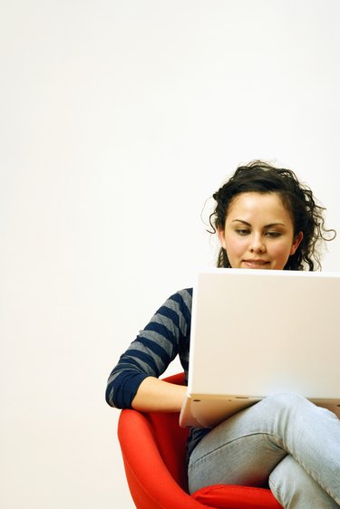 Girl (14-15) using laptop, sitting on chair, smiling