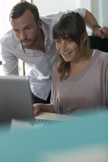 two people at desk look at computer