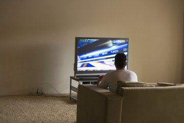 Young man sitting on sofa watching tv, rear view