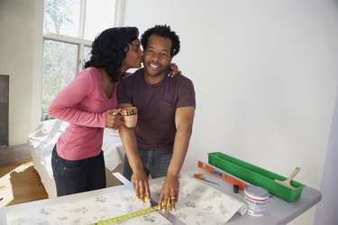 African man measuring wall paper getting kiss from wife