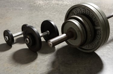 Two dumbbells and barbell side by side on concrete floor