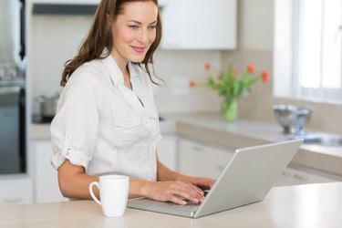 Smiling young woman using laptop in kitchen