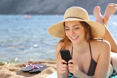 Woman on the beach texting a smart phone in summer