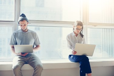 Man and woman with laptops near big bright window