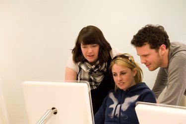 Group of three graphic design students working together on a mac computer.