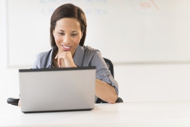 Businesswoman With Hand On Chin Using Laptop At Desk