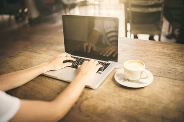 Girl typing on a laptop keyboard in a cafe