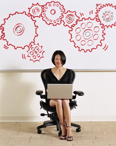 Woman using laptop, illustrated cogs on whiteboard in background