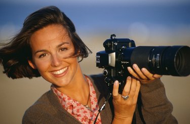 Woman holding camera with telephoto lens, smiling, portrait