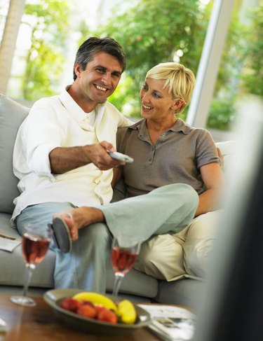 Couple sitting on sofa, man holding remote control, smiling