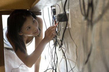 Asian woman looking at plugs under desk