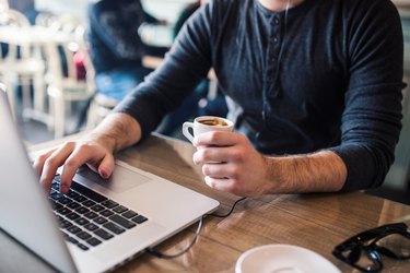 Man holding coffe in one hand and working on laptop