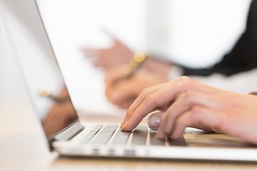 Woman using laptop in office during a meeting. Close-up hands