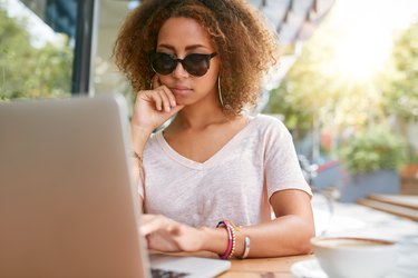 Stylish young girl at outdoor cafe using laptop