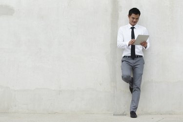 Young businessman reading while leaning on a blank wall