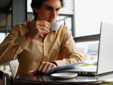 Young businessman using laptop sitting at table drinking coffee