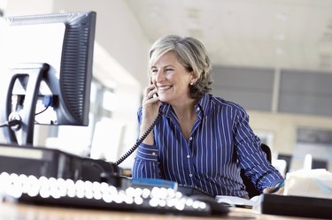 Mature woman using telephone at desk in office, smiling