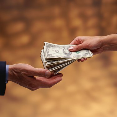 Woman's hand giving stack of US $20 bills to man's hand