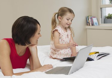 Mother and daughter drawing and using laptop on bed