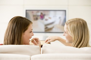 Two women in living room watching television eating chocolates