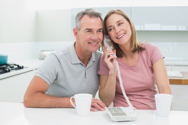Happy couple using landline phone together in kitchen