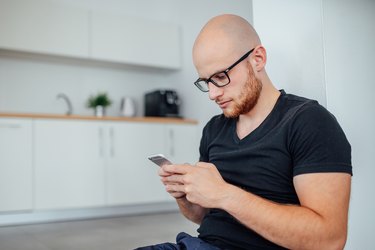 Man is sitting and using mobile phone. Kitchen background.
