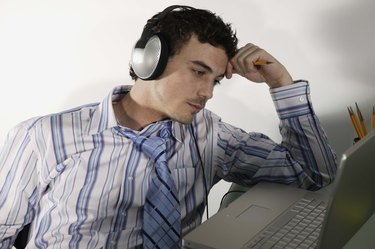 Bored businessman using laptop while listening to music