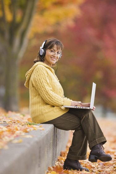 Hispanic woman using laptop outdoors with headphones