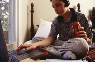 Teenage boy (16-17) using laptop, sitting on bed