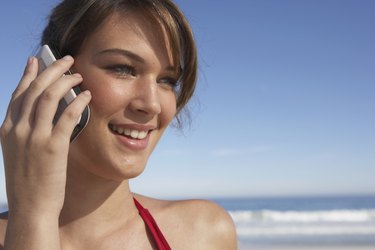 Young woman using mobile phone, outdoors, smiling, close-up