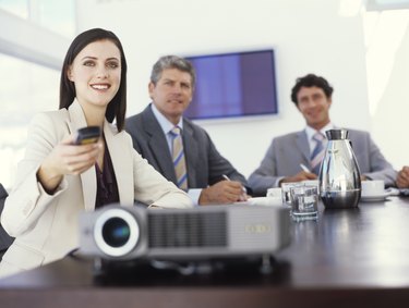 Projector on table, businesswoman using remote