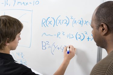 Student writing maths equations on whiteboard with tutor