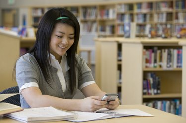 School girl (14-15) text messaging in library