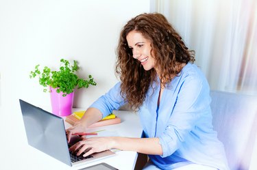 Smiling young woman siting at table and using laptop.
