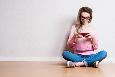 Happy beautiful woman sitting on the floor and using smartphone