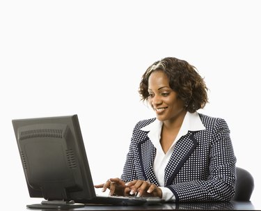 Smiling businesswoman sitting at desk typing on computer.