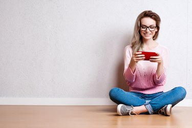 Happy beautiful woman sitting on the floor and using smartphone
