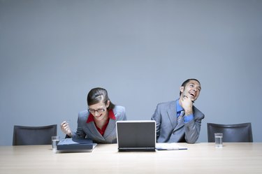 Businesswoman and businessman sitting at desk with laptop, laughing