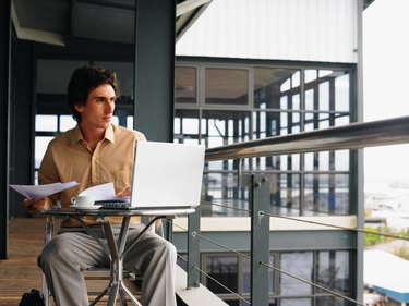 Young businessman using laptop sitting at table on balcony