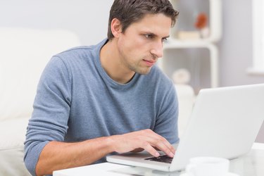 Serious young man using laptop in living room