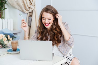 Cheerful woman using laptop and eating lollipop in cafe