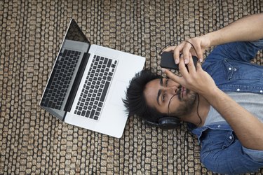 Asian man lying on the floor with laptop and phone.