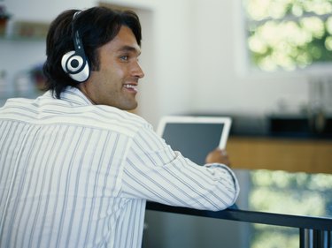 Young man wearing headphones using laptop, looking away, rear view